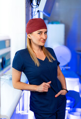 Doc confidently poses in clinic. A healthcare worker stands at a treatment area wearing scrubs and...