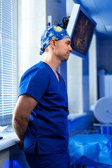 Surgeon readying for surgery. A focused surgeon stands by a window in scrubs, ready for an upcoming...