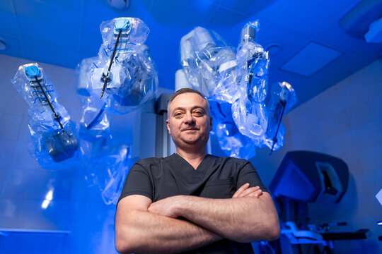 Surgeon in front of robotic equipment. Surgeon stands confidently in a modern operating room with robotic surgical instruments illuminated by blue lights.