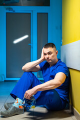 Healthcare worker resting in a hallway. A tired healthcare worker in scrubs and colorful socks sits...
