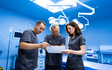 Surgery plans discussed in OR. Three medical professionals review a document together in a bright...