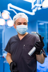 Surgeon gets ready for surgery. A surgeon in scrubs and gloves holds a surgical tool, ready for an...