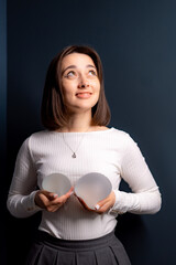 Woman with silicone implants indoors. A young woman stands in a dimly lit room, holding two...