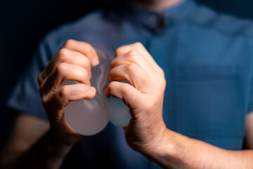Hands grip clear items in darkness. Two hands grip and apply pressure to two translucent objects, creating an impression of strength and focus.