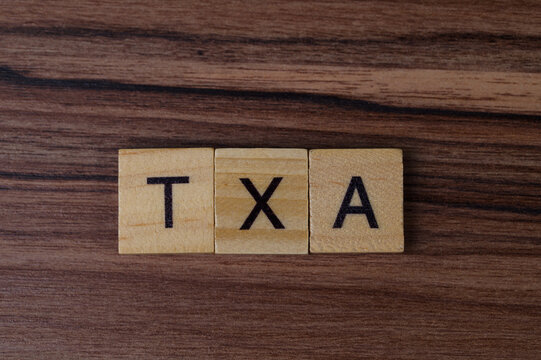 Wooden Scrabble Tiles Arranged to Spell TXA on a Wooden Surface