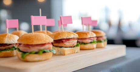 Delicious mini sliders on a wooden board, each adorned with a pink flag, ready to be enjoyed at a gathering or event. Close up view.
