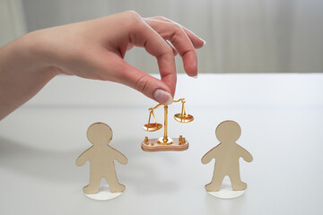 A hand holds a scale of justice between two figures of people. Concept of justice, equality, decision making, verdict, mediation in disputes, lawyer, jurisprudence, problem solving