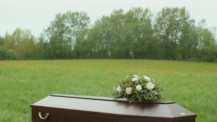 Slowmo shot of sad young Caucasian man wearing black coat looking at closed casket and then going away being last one to leave outdoor funeral ceremony