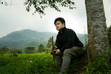A man stands in a dense tropical forest holding a camera, surrounded by greenery and natural...