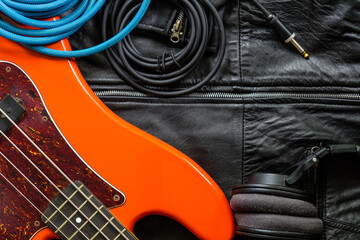 orange electric bass guitar, headphones and cable on a black leather jacket background.