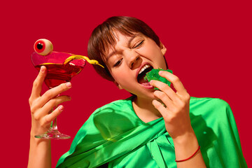 Woman biting green jelly with cocktail and gummy eyeball in humorous food setting. Concept of surreal snack visuals, candy rebellion, emotional indulgence, pop youth culture.