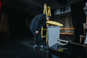A theatrical performance featuring an actor engaging with stage props during a play on a dimly-lit...