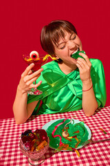 Woman aggressively eating jelly and holding cocktail with eyeball and candy worms. Concept of bold...