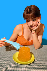 Bored woman poking jelly with blue toy claw on birthday table in orange top. Concept of ironic...