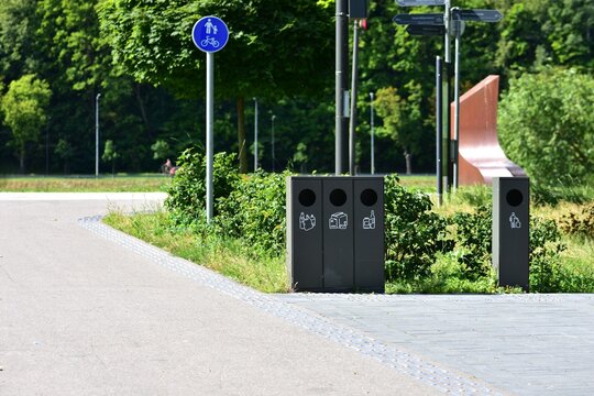 Modern waste sorting bins along city sidewalk near park. Eco-friendly recycling station encourages sustainability and clean public spaces. Clear labels guide proper waste disposal.