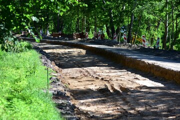 Dug-out road under reconstruction in green forested area. Graded dirt surface and tire marks show...