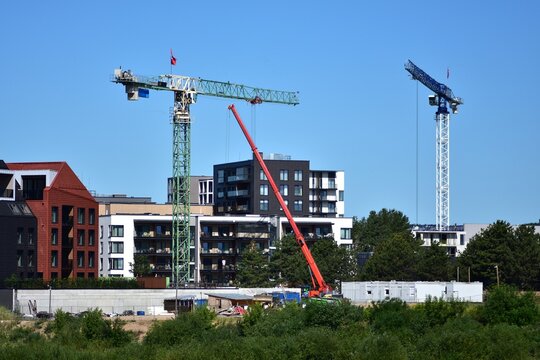Cranes and construction site in modern city district. Apartment buildings rise behind machinery under clear blue sky. Urban growth, development, and real estate expansion captured. - Powered by Adobe