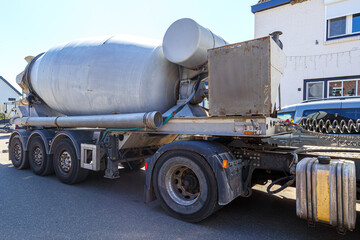 Mixer tank of a concrete mixer truck parked on village street, wheels, hoses, cleaning system and electrical equipment, sunny day in Gulpen, South Limburg, Netherlands