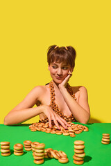 Smirking woman arranging ring snacks on table wearing playful bagel bikini. Concept of quirky snack...