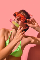 Cheerful woman in neon bikini biting rainbow popsicle with oversized sunglasses. Concept of summer...
