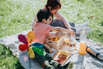 A Filipino mother and her young child share a picnic on a sunny day in a vibrant park. They enjoy...