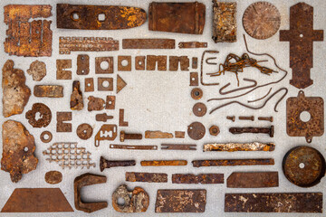 A group of various old rusty bits and pieces arranged on a concrete surface. Old rusty nuts, bolts, nails and other parts flay lay on gray background.