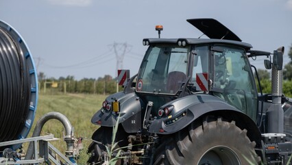 Fototapeta premium Modern black tractor with irrigation equipment on farmland