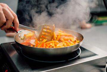 A skilled chef stirfries colorful vegetables on an electric stove, creating a truly delicious dish