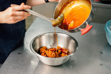 A talented chef is carefully pouring a rich, flavorful sauce over succulent cooked chicken in a...