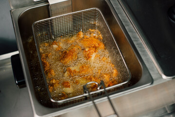 Fresh chicken pieces are frying in hot oil, creating a wonderfully golden crispy texture in a commercial fryer