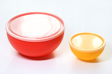 A close-up view of two empty, colorful plastic food containers with clear lids, one red and one...
