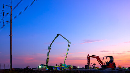Concrete pump truck with construction workers group are working overtime to pouring concrete floor in industrial factory building site area against colorful dusk sky background