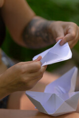 A woman is gently holding an intricately folded origami boat carefully in her hands, showcasing the...