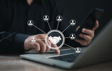 Business professional using smartphone and laptop initiates virtual handshake with connected icons, symbolizing digital networking, partnership building, and collaborative business communication.