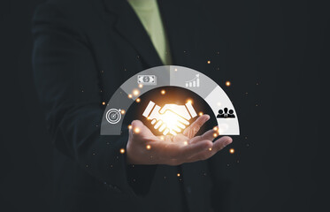 Businessman presenting glowing handshake icon surrounded by business, finance, and collaboration symbols, representing successful partnership, strategic cooperation, and trust in modern alliances.
