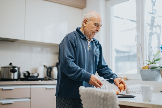 An elderly man peeling onions while preparing food in a well-lit and modern kitchen, depicting a moment of daily routine and self-sufficiency.