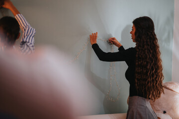 A family decorates their home for a birthday party, carefully arranging string lights. This warm...