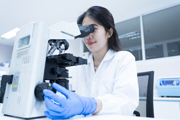 Selective focus woman Asian scientist using microscope to analyze blood smear slide sample at labolatory room.Specialist development and production of new medicines.