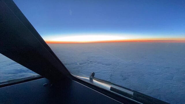 Dramatic time-lapse from a commercial airline cockpit showing sunrise along the horizon during a North Atlantic crossing. The glowing orange horizon above an expansive cloud layer captures the unique 