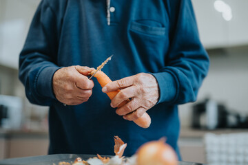 Elderly man thoughtfully preparing vegetables by peeling a carrot in a warm kitchen setting,...