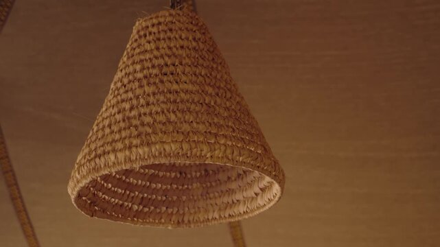 Close-up of a wicker lampshade hanging from the ceiling of a tent in Morocco. The light casts a warm glow, creating a cozy atmosphere. Ideal for projects related to travel, culture, interior design