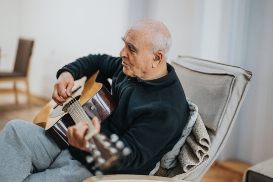 An older adult enjoying a moment of music by strumming an acoustic guitar in a relaxing indoor setting, expressing joy and creativity.