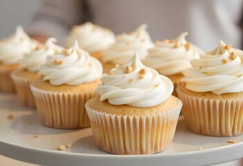 Freshly baked vanilla cupcakes topped with smooth white frosting and a sprinkle of nuts, arranged neatly on a white tray