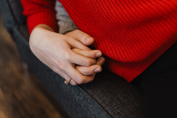 Close-up of two people holding hands while sitting on a couch, one wearing a red sweater and gold...
