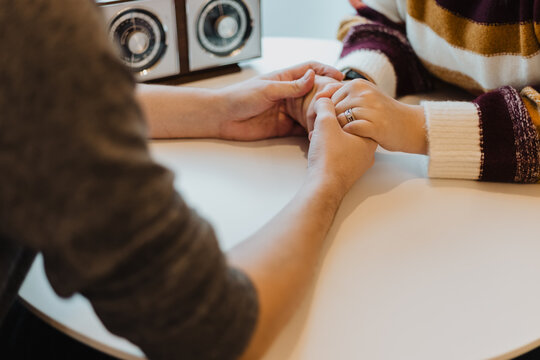 Close-up of couple holding hands across a round table, symbolizing emotional support and connection - Powered by Adobe