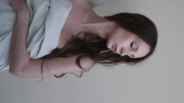 Portrait of a beautiful brunette with long hair on a fabric background in the studio. Beautiful natural woman posing for the camera