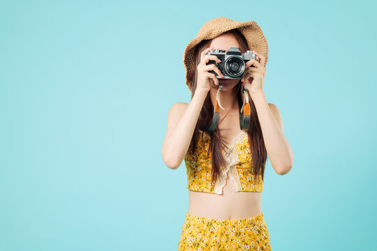 Happy asian tourist woman photo taking with camera and hat on travel, enjoying her summer holiday vacation, smiling as she captures memories on her travel, headshots isolated studio blue background