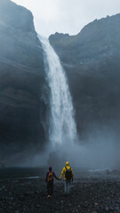 A couple holds hands while walking towards the majestic Haifoss waterfall in Iceland.