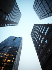 Naklejka premium Upward wide-angle view of modern corporate skyscrapers with glass reflections and open blue sky, symbolizing business growth, financial ambition, and real estate development in urban city centers.