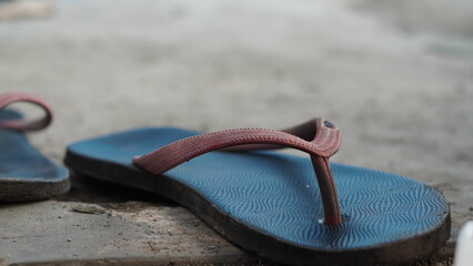 Detailed close-up of a dusty blue flip flop with red straps placed on a rough concrete floor,...